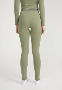 Leggings verde oliva realizzati in tessuto morbido e elasticizzato con vita alta, caratterizzati da una superficie liscia e una silhouette aderente.