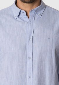 Camisa de botones en azul claro, fabricada en un tejido ligero, con una sutil textura a rayas. Presenta un cuello abotonado y un logotipo bordado.