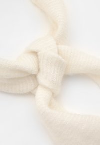 Knutig krämfärgad tygband, tillverkad av mjukt, texturerat material med en lätt lyster, med en tvinnad design.