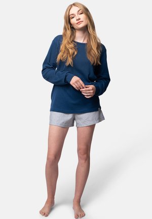 Maglia a maniche lunghe a coste blu navy abbinata a pantaloni corti a righe bianche e blu, con una vestibilità morbida e rilassata. Posizione eretta, a piedi nudi.