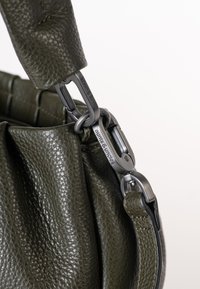 Olijfgroene leren handtas met een gestructureerd oppervlak, voorzien van een zilverkleurige metalen sluiting en een gevlochten schouderband.