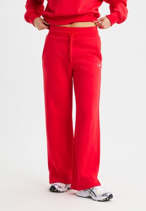 Rode sweatpants met een trekkoord in de taille, wijde pijpen en zijzakken. Glad stofoppervlak, met een klein logo op de dij.