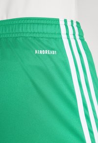 Zelené športové šortky s hladkou textúrou, s tromi bielymi pruhmi na boku a logom "AEROREADY" na prednej strane.