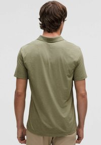 Oliwkowa koszulka polo z krótkim rękawem, kołnierzykiem i prostym krojem. Miękka tekstura z delikatnymi przeszyciami na ramionach.