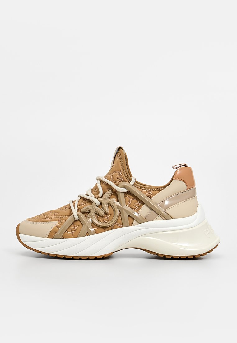 Chaussures de sport beige et tan avec un tissu texturé, des coutures décoratives, des accents en cuir lisse, une épaisse semelle blanche et un détail de lacets circulaires.