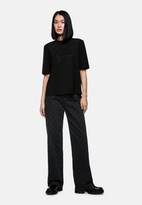 Black t-shirt with a rounded logo design, paired with loose, black patterned pants featuring star motifs. Shoes have a shiny finish.