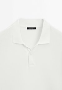 Polo blanc à manches courtes avec col et deux boutons, comportant une étiquette noire à l'intérieur de l'encolure.