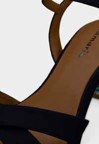 Gros plan sur la semelle intérieure en cuir marron avec des brides en daim noir d'une sandale pour femmes, montrant une partie de la bride de cheville et les détails de couture.