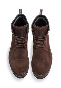 Bottines en suède marron avec un bout arrondi, des accents en cuir noir contrastants, une languette en tissu et des lacets à l'avant pour la fermeture.
