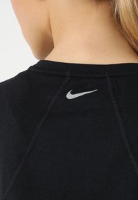 Camiseta deportiva negra con cuello redondo, logo plateado de Nike en la parte posterior y costuras visibles. Textura de tela suave y elástica.