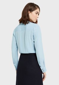 Světle modrá blůza s dlouhým rukávem, límečkem, hladkou texturou a manžetami na knoflíky, doplněná tmavou sukní.