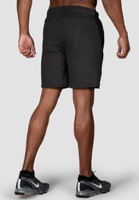 Gray athletic shorts with an elastic waistband, smooth texture, and side pockets, paired with black and gray sneakers.