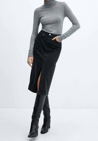 Suéter de cuello alto gris combinado con una falda midi de mezclilla negra que presenta una abertura lateral alta, llevada con botas de tacón negro hasta la rodilla.