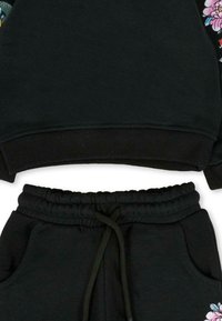 Schwarzer Sweatshirt mit Blumenmuster an den Ärmeln, gerippte Bündchen und passende Sweatpants mit seitlichen Taschen und elastischem Bund.
