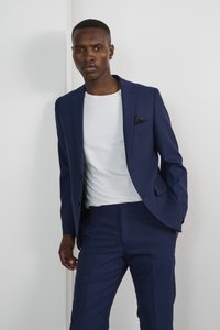 Traje azul marino con un corte a medida y una textura sutil, combinado con una camiseta de cuello redondo blanca. Pañuelo de bolsillo visible en el bolsillo del pecho de la chaqueta.