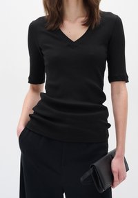 Svart ribbad stickad topp med V-ringning och veckade korta ärmar, kombinerad med svarta byxor och en svart kuvertväska. Enkelt mönster och textur.