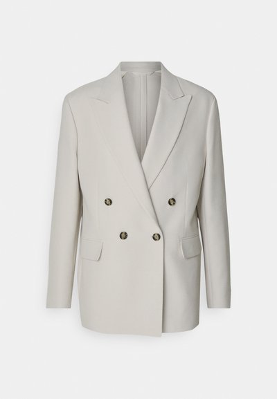 Blazer beige clair à double boutonnage avec poignées en pointe, deux poches avant et boutons ronds foncés. Tissu lisse, coupe ajustée.