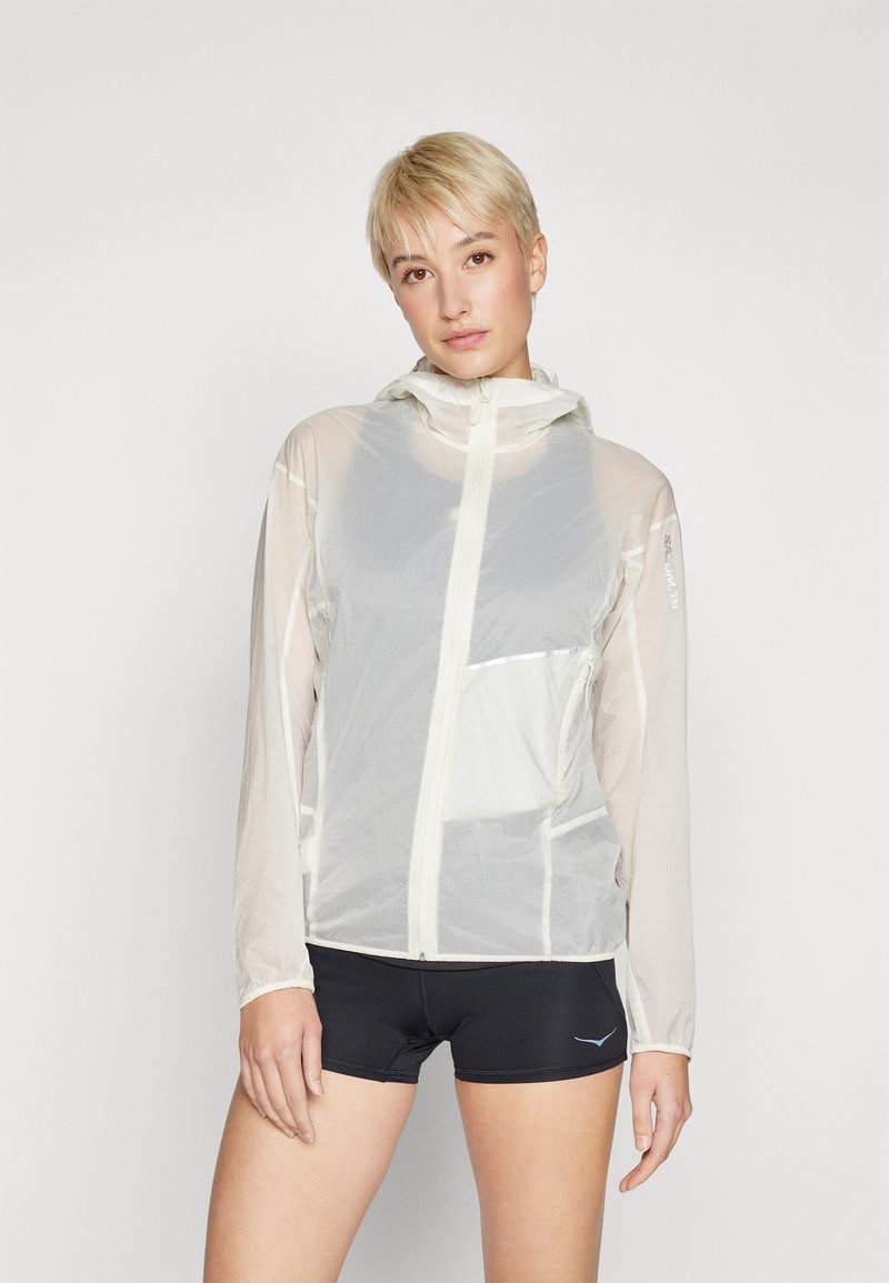 Lightweight, translucent jacket in off-white with a front zipper, adjustable hood, and reflective accents. Features long sleeves and a pocket.