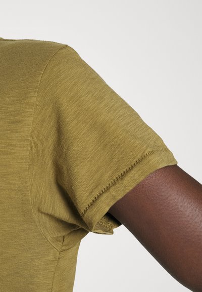 Olive green short-sleeved shirt with a smooth texture, featuring a raw edge hem and a round neckline. The sleeve is slightly relaxed.