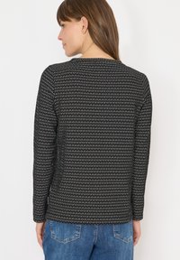 Top lungo a maniche nere con motivo, dotato di scollatura rotonda, realizzato in tessuto a maglia testurizzato e con taglio dritto, abbinato a jeans blu.