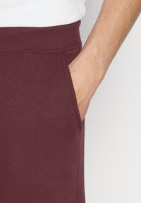Burgundy sweatpants with a ribbed waistband, side pockets, and a soft texture. The design features a casual fit and smooth fabric.