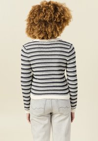Suéter a rayas en crema y navy con puños y dobladillo acanalados. Textura de punto con líneas horizontales alternadas. Lleva puesto unos jeans gris claro.