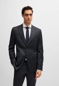 Navy suiting with a textured finish, featuring a single-button blazer, notch lapels, and slim-fit trousers. Accessories include a white shirt and dark tie.