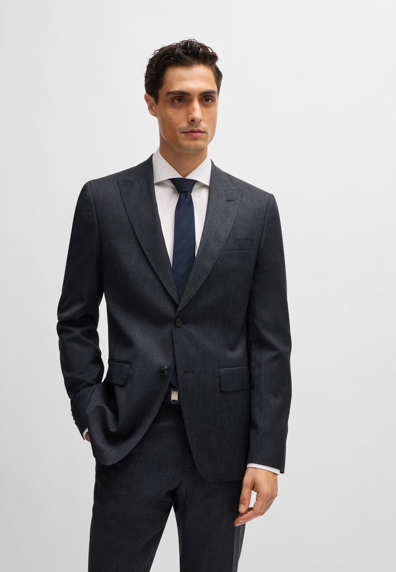 Navy suiting with a textured finish, featuring a single-button blazer, notch lapels, and slim-fit trousers. Accessories include a white shirt and dark tie.