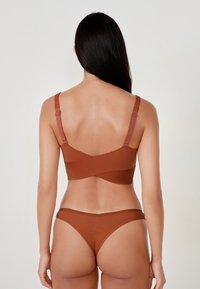 Completo di reggiseno a coste marrone e perizoma coordinato, con spalline regolabili e design incrociato sulla schiena. Textura liscia con accenti minimalisti.