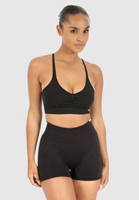 Sostén deportivo negro con tirantes finos y detalle fruncido en el centro; pantalones cortos negros de tiro alto hechos de tela elástica; textura suave.
