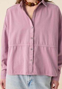 Pink button-up shirt with a relaxed fit, long sleeves, and silver snap buttons. The fabric shows a soft texture with visible seams.