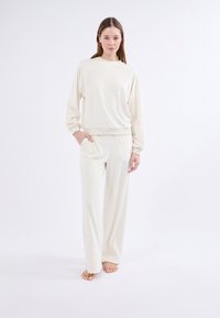 Set di abbigliamento da casa color crema composto da una felpa ampia con colletto rotondo e maniche larghe, abbinata a pantaloni larghi coordinati.