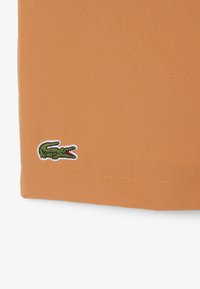 Pantaloncini di tessuto arancione con finitura strutturata. Piccolo logo del coccodrillo verde ricamato all'orlo. Design semplice e senza decorazioni.