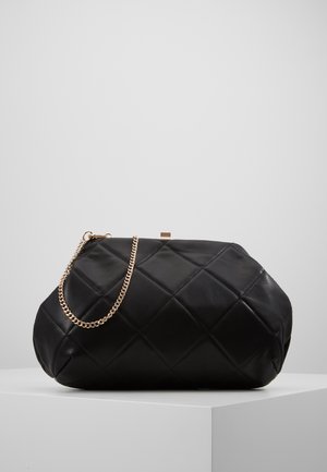 Borsa clutch in pelle nera trapuntata con tracolla a catena dorata appoggiata su un piedistallo bianco su sfondo grigio uniforme.