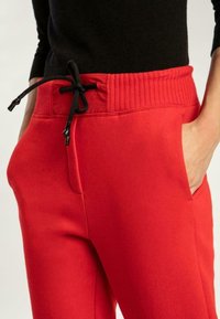 Rode sweatpants met een geribde tailleband, zwarte trekkoord en zijzakken. Gladde stof met een ontspannen pasvorm ontwerp.