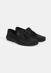 Schwarze Leder-Mokassins mit strukturiertem Obermaterial, dekorativen Quasten und einer flachen Gummisohle. Abgerundete Spitze mit genähten Details.