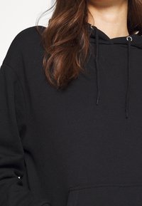 Svart bomullshuvtröja med kenguruficka, justerbar dragsko och en mjuk textur. Har avslappnad passform och ribbade muddar.