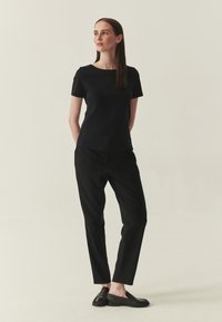 Haut noir à manches courtes avec un col rond, associé à un pantalon noir fuselé et des chaussures noires à enfiler, présentant une texture lisse et élégante.