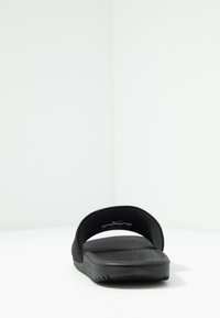 Sort slide sandal med bred rem og tekstureret fodseng. Flad sål med ribbet design for greb. Minimalistisk stil, ingen yderligere accenter.