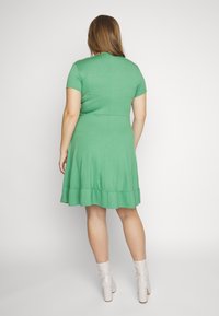 Vestido verde de manga curta com saia rodada e bainha com pregas. Feito de tecido suave, apresenta um corpete ajustado e detalhes sutis na costura traseira.