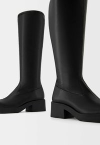 Black knee-high boots crafted from smooth leather, featuring a block heel and subtle stitching detail on the upper for added texture.