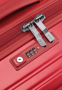 Valigia rigida rossa con doppizie cerniere metalliche, manico in plastica, lucchetto a combinazione e un foro per chiave, caratterizzata da una superficie liscia e accenti sottili.