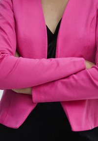 Tajmad rosa kavaj med mjuk textur, öppen front och långa ärmar, lager över en svart topp. Inga synliga knappar eller dekorationer.