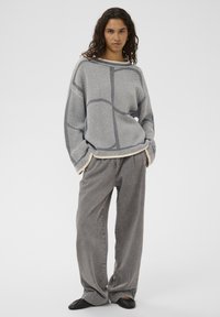 Pull gris surdimensionné avec un tricot texturé, présentant un motif en grille. Associé à un pantalon gris ample et des chaussures plates noires.
