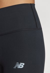Mustat urheilulegginsit, joissa on tiukka muotoilu, valmistettu sileästä kankaasta, jossa on heijastava logo ja litteä, ommeltu vyötärönauha.