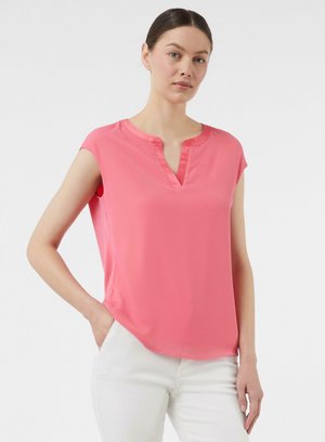 Roze blouse met korte mouwen en een V-hals, gemaakt van een soepele stof. Heeft subtiele zij-spleten en een losse pasvorm. Gecombineerd met witte broeken.