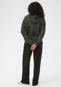 Grijze textuur gebreide hoodie met een capuchon, gecombineerd met zwarte wijde broek en witte schoenen. De achterkant toont een relaxte pasvorm en ribgebreide manchetten.