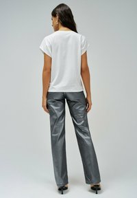 Bijela majica kratkih rukava uparena s sjajnim, srebrnim hlačama širokih nogavica. Ovaj outfit ima elegantnu teksturu i minimalistički dizajn.