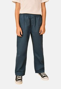 Modré bavlnené nohavice s elastickým pásom, rovnými nohavicami a bočnými kapsami, skombinované s čiernymi teniskami s bielymi šnúrkami.