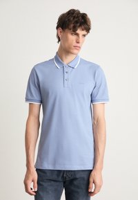 Polo majica v svetlo modri bombažni tkanini z ovratnikom, трими gumbi in belimi detajli na ovratniku in rokavih.